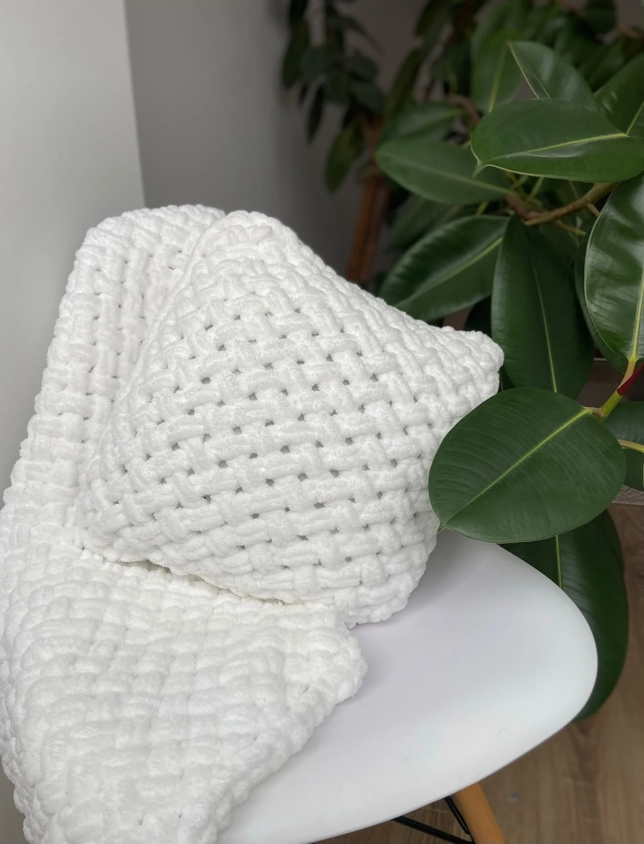 White handmade blanket with a basket weave texture beside a green plant