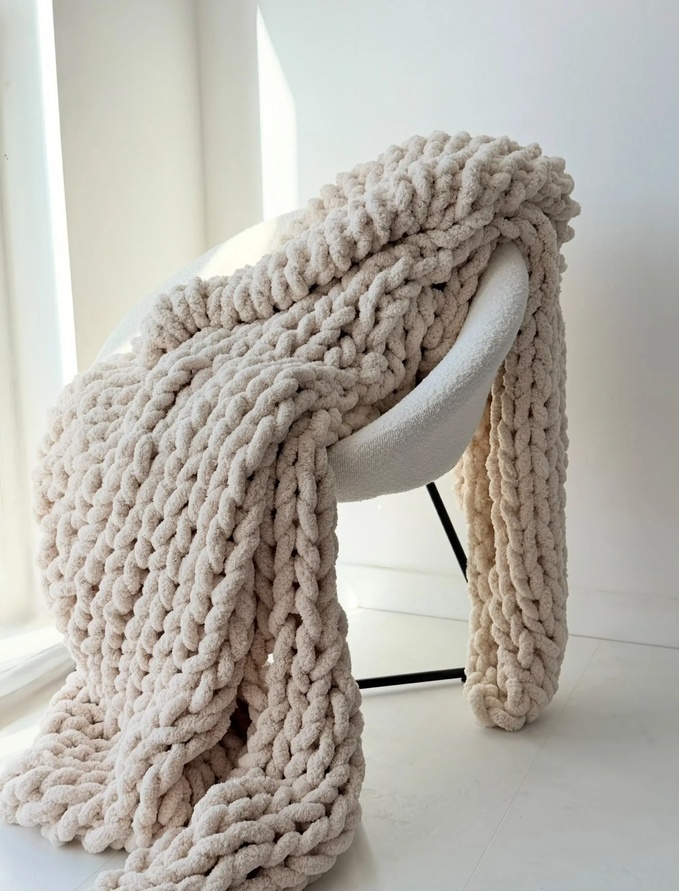 Neutral handmade blanket with a chunky braided texture draped over a white chair in natural light
